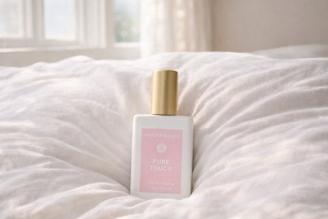 Pure Touch άρωμα NATURA DANZA πάνω σε λευκά σεντόνια με πρωινό φως.