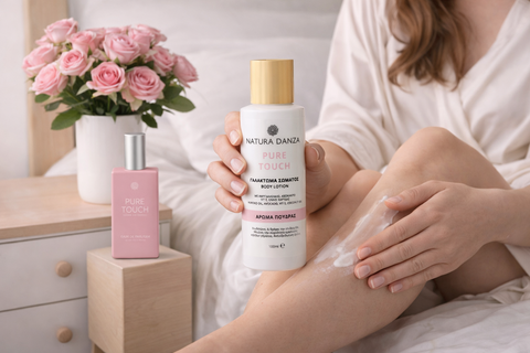 γυναίκα εφαρμόζει γαλάκτωμα σώματος Pure Touch της NATURA DANZA στα πόδια σε κρεβάτι με ροζ τριαντάφυλλα στο κομοδίνο